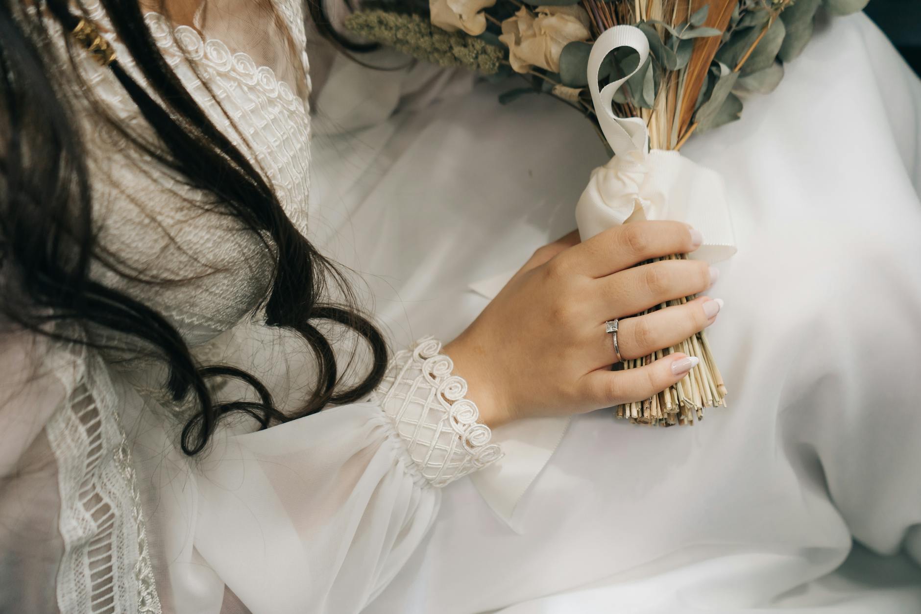 Close-up of a bride's hand holding a bouquet, showcasing detailed lace on a wedding dress. - wedding day anxiety