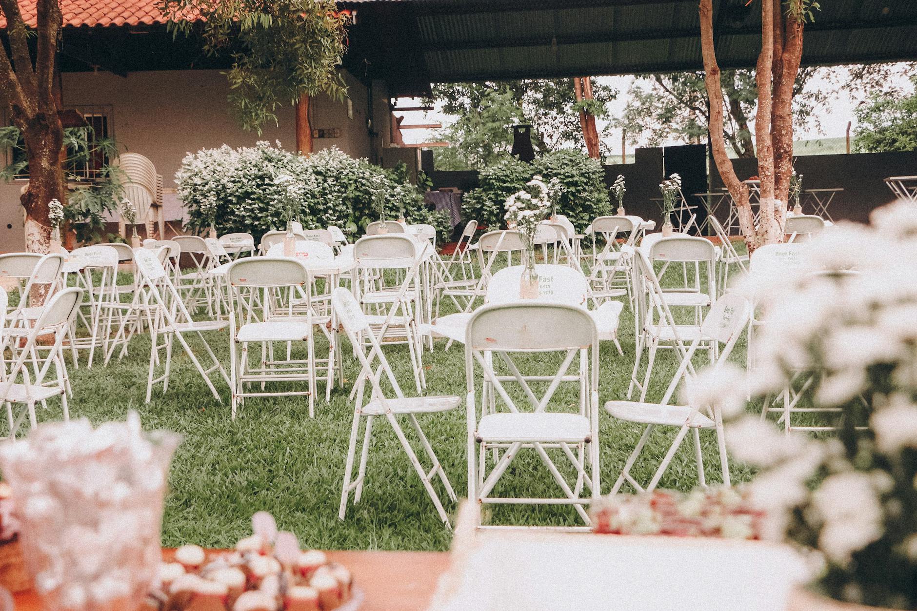 An outdoor wedding venue setup with white folding chairs on green grass and decorative plants. - wedding planning stress