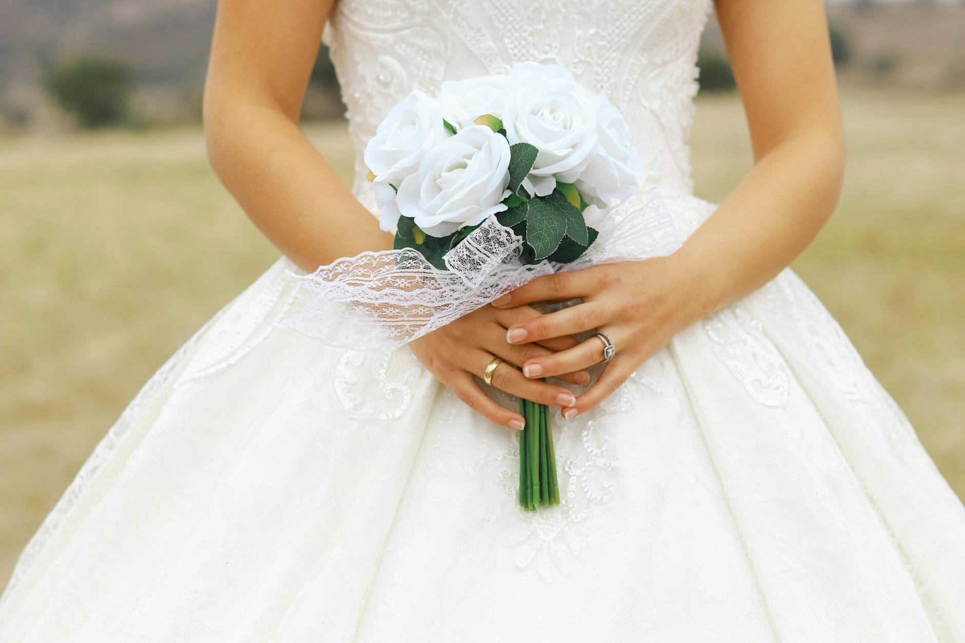 A bride in a white dress holding a bouquet of white roses against an outdoor backdrop, showcasing elegance and charm. - wedding stress management