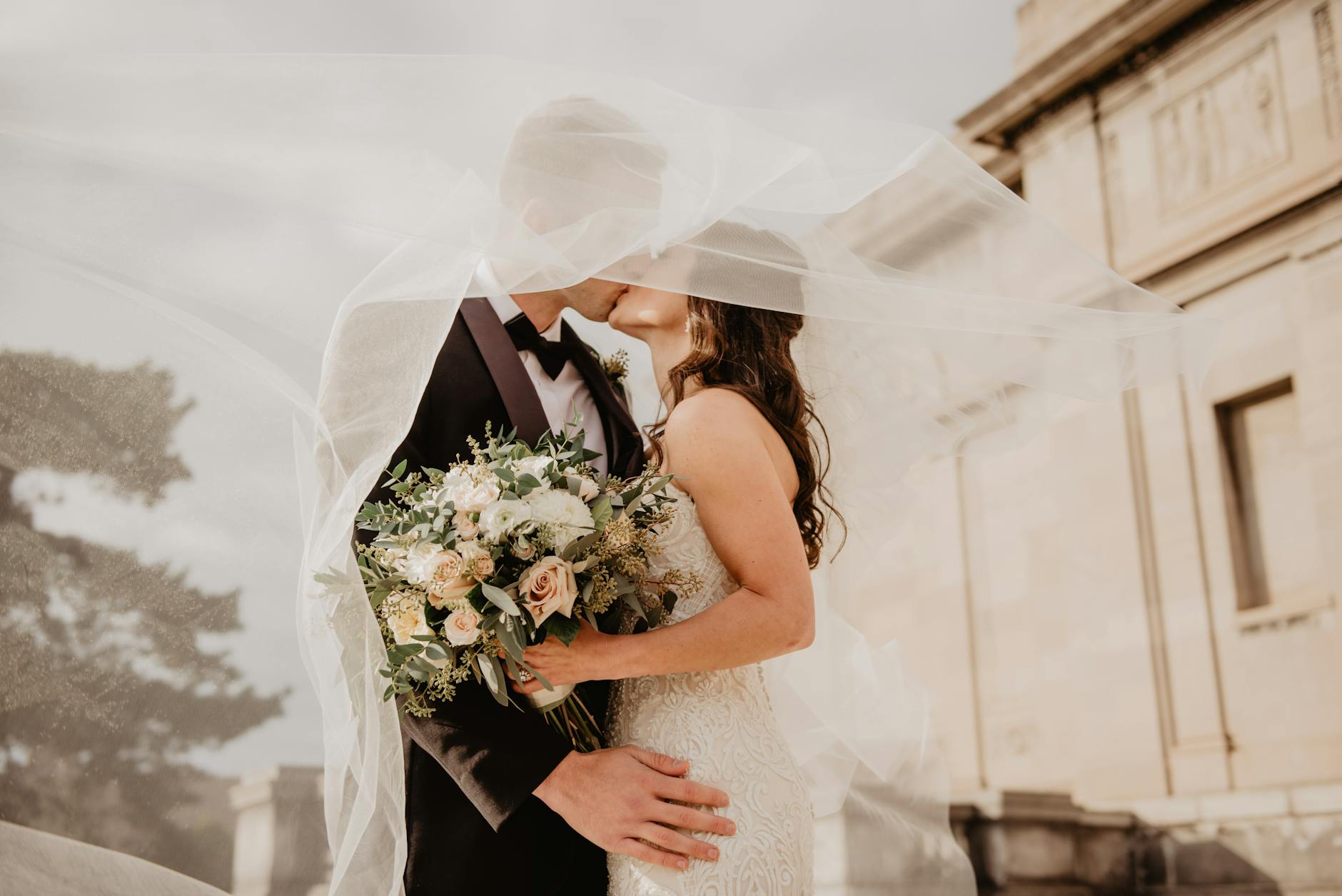 Bride and groom share a tender kiss under a veil, showcasing love and romance on their special day. - wedding stress relief